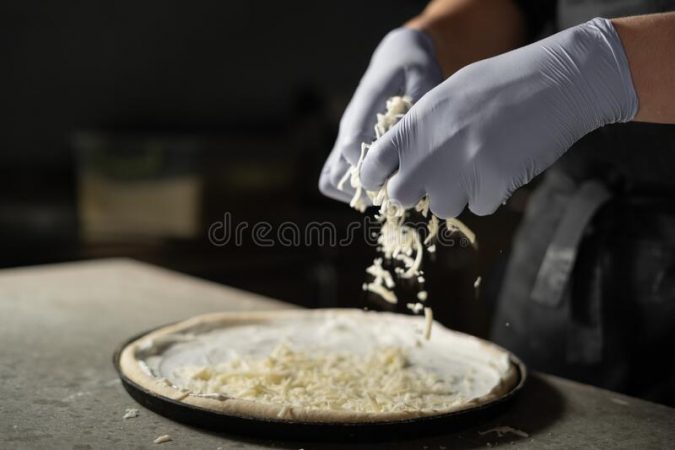 los cocineros guantes manos espolvorear queso rallado en una pizza cruda redonda hornear pizzeria el concepto de cocina un 207695388 Merca2.es