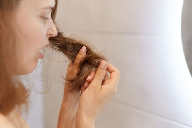 closeup retrato perfil mujer sorprendida molesta que mira su cabello seco tiene problemas necesita cambiar champu o tratamiento especial clinica tricologica Merca2.es