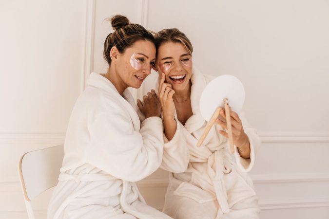 cute caucasian young women bathrobes admire themselves while looking mirror white background beauty personal care skin face care concept Merca2.es