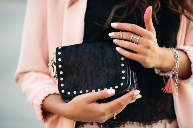 female hands with beautiful nail polish rings holding small black bag Merca2.es