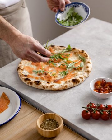 high angle man putting arugula baked pizza dough with smoked salmon slices Merca2.es