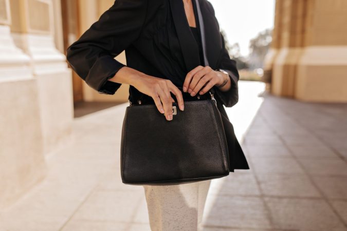 woman black jacket white trousers holding dark handbag outside woman modern clothes posing with stylish bag outdoors Merca2.es