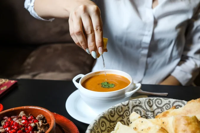 woman squeeze lemon into lentil soup side view Merca2.es