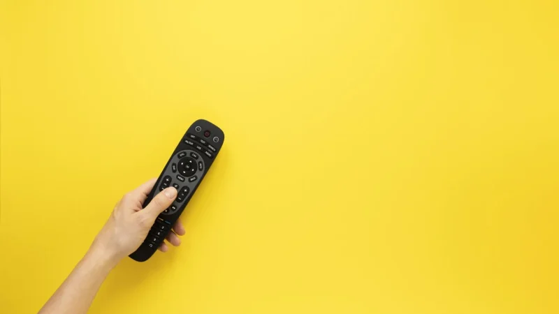 person holding remote yellow background with copy space Merca2.es
