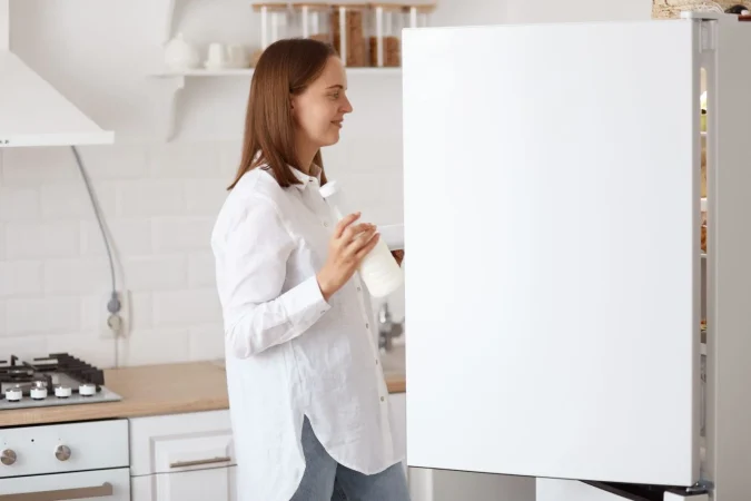 ¿Sabes qué significan los números de las neveras? No indican lo que te crees 2 Merca2.es profile portrait attractive dark haired woman wearing white shirt looking smiling inside fridge with positive emotions holding plate hands posing with kitchen set background Merca2.es