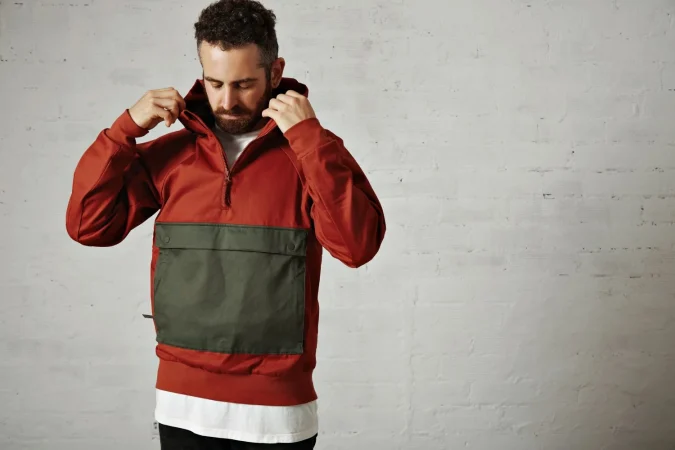 young man with beard putting hood his stylish red grey anorack isolated white Merca2.es