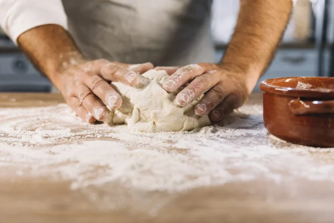 Cómo hacer la masa de pizza al estilo de la Nonna: Un viaje a la auténtica cocina italiana 4 Merca2.es panadero de sexo masculino amasando la harina de la masa en la mesa de madera Merca2.es