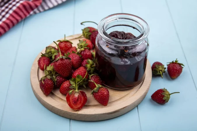 Cómo hacer mermelada de fresa casera como la de las abuelas 5 Merca2.es vista superior de mermelada de fresa con fresas frescas en una tabla de cocina de madera sobre un fondo azul Merca2.es