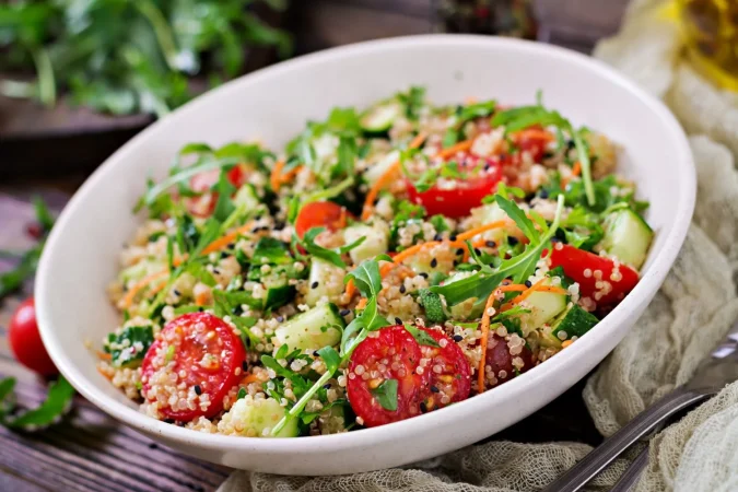 Ensalada de quinoa, pollo y verduras: Una explosión de sabor, frescor y nutrición 3 Merca2.es ensaladas con quinua rucula rabano tomate y pepino en un recipiente en la mesa de madera comida sana dieta desintoxicacion y concepto vegetariano Merca2.es
