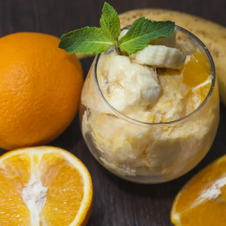 fruta de platano y naranja con menta en vaso con frutas enteras en mesa de madera Merca2.es
