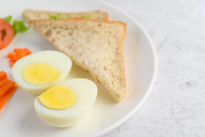 huevos cocidos pan zanahorias y tomates en un plato blanco con cuchillo y tenedor Merca2.es