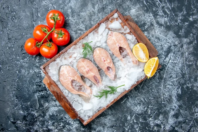 vista superior rebanadas de pescado crudo con hielo en tablero de madera tomates frescos en el espacio libre de la mesa Merca2.es