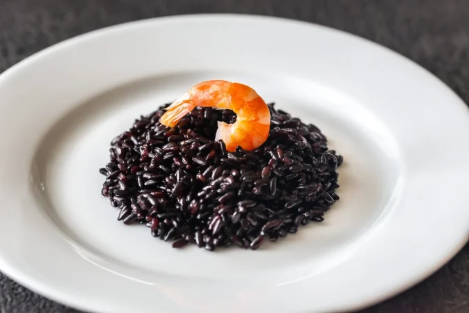 arroz negro con camarones en plato blanco Merca2.es