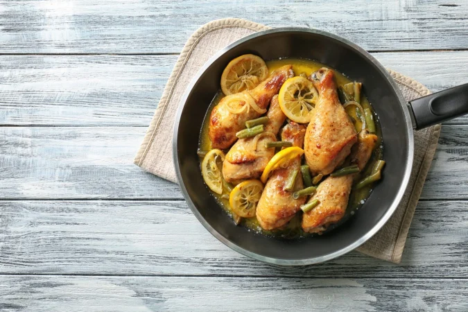 deliciosos muslos de pollo con limon en sarten sobre mesa de madera Merca2.es