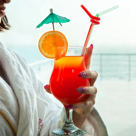 mujer que sostiene el coctel rojo que mira afuera de ventana en albornoz Merca2.es