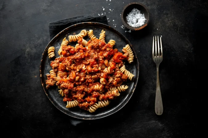 pasta con salsa bolonesa servida en plato sobre fondo oscuro Merca2.es