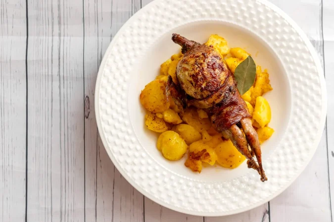 codorniz asada envuelta en tocino con hierbas en una sarten Merca2.es