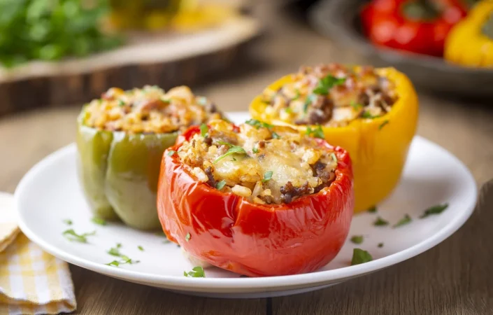 pimientos rellenos mitades de pimientos rellenos con arroz tomates secos hierbas y queso en una fuente para horno sobre una mesa de madera azul vista superior nombre turco biber dolmasi Merca2.es