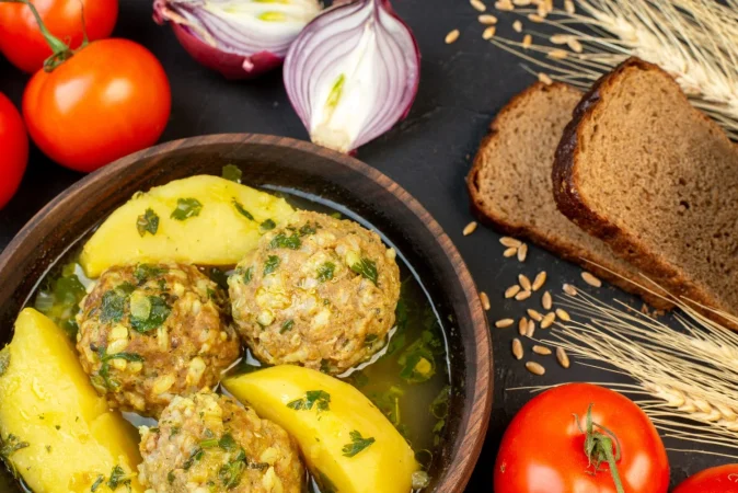 vista de cerca de rebanadas de pan negro deliciosa comida de albondigas con patatas verdes y verduras frescas sobre fondo negro Merca2.es