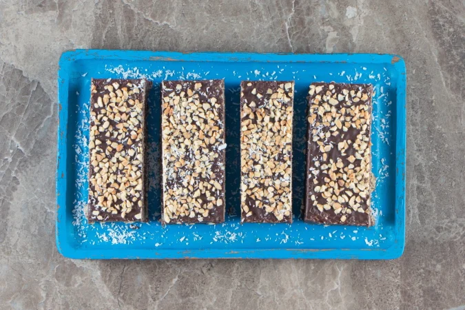 barra de chocolate en rodajas con nueces sobre placa de madera sobre marmol Merca2.es