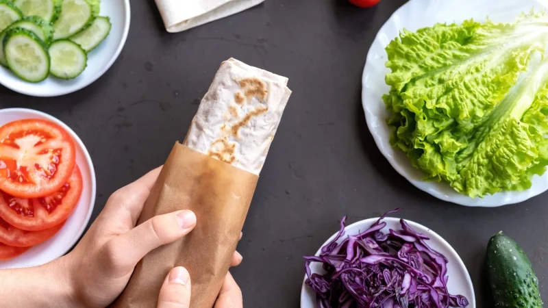 Burrito de pollo y verduras: la receta fácil que conquista medio mundo (y sus curiosidades más sorprendentes) 30 Merca2.es composicion de alimentos saludables verduras en platos y manos masculinas sosteniendo un rollo de pita Merca2.es