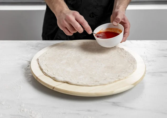 hombre de alto angulo esparcir salsa de tomate sobre masa de pizza Merca2.es