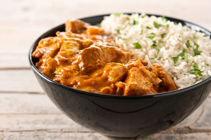 Pollo al curry: receta, secretos y curiosidades del plato que conquista a medio mundo 1 Merca2.es pollo de mantequilla india en tazon negro sobre mesa de madera Merca2.es