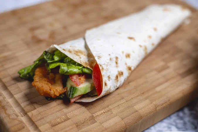 Burrito de pollo y verduras: la receta fácil que conquista medio mundo (y sus curiosidades más sorprendentes) 32 Merca2.es vista lateral rollito de pollo filete de pollo frito con tomate pepino y lechuga en pita Merca2.es