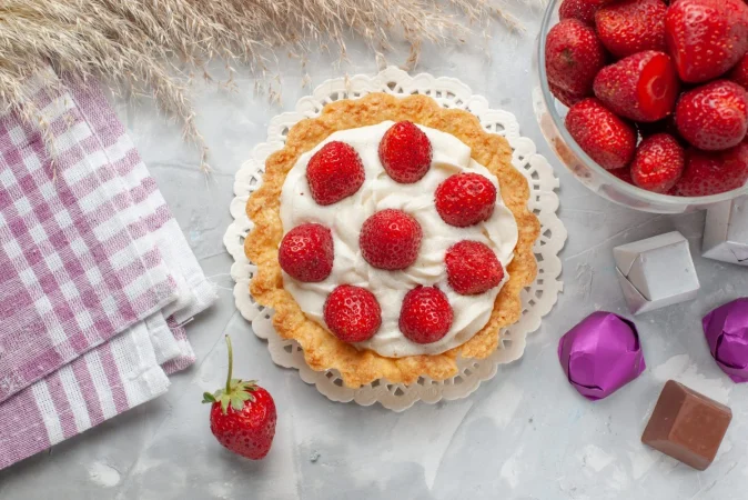 vista superior pequeno pastel cremoso con fresas rojas frescas y caramelos de chocolate en el escritorio de luz blanca pastel crema de galletas de frutas y bayas Merca2.es